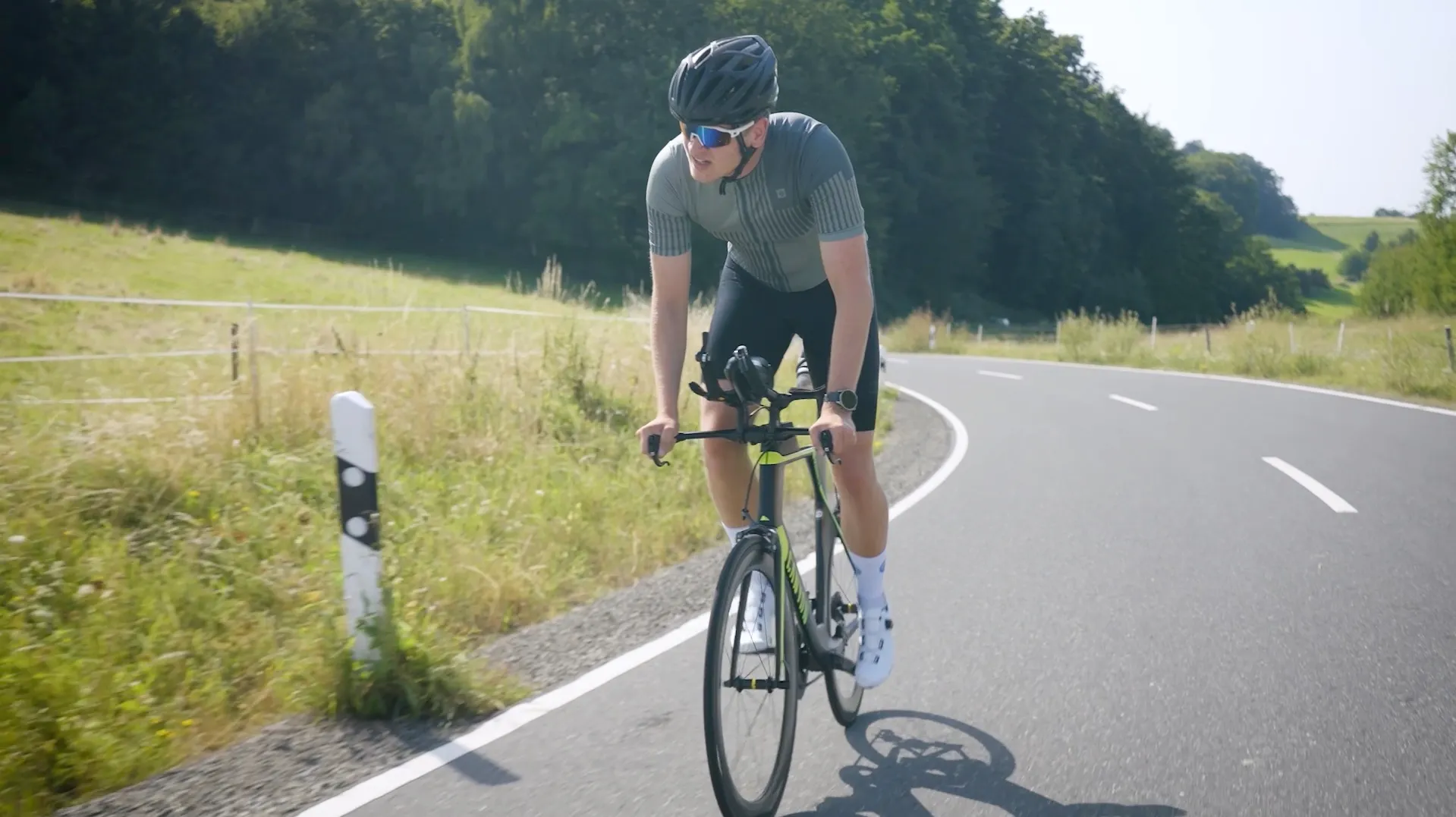 Pascal Kayser mit Helm und Sonnenbrille auf dem Rennrad, unterwegs auf einer Landstraße zwischen Wiesen