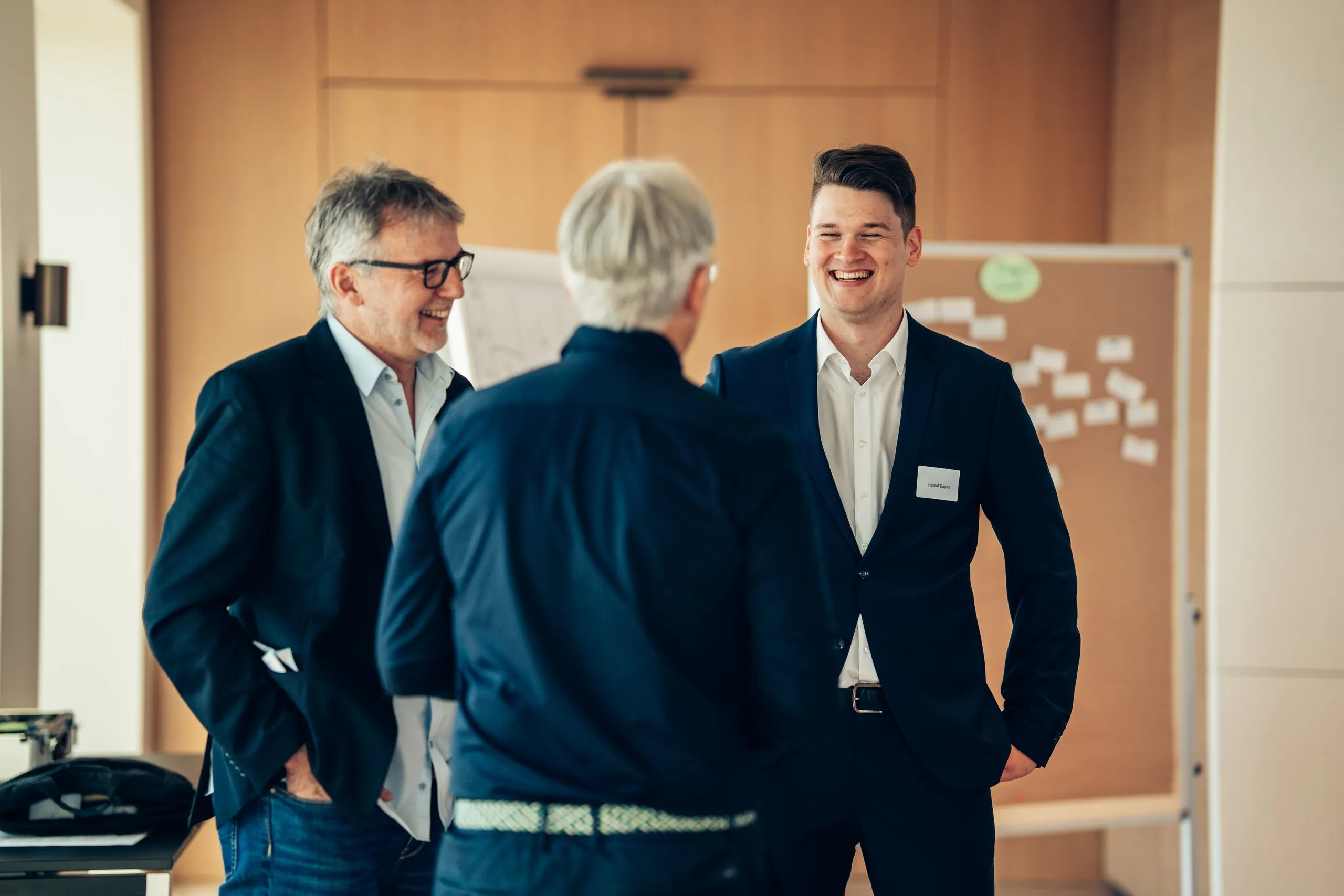 Pascal Kayser lacht im Austausch mit zwei Teilnehmern vor einer Pinnwand im Workshop